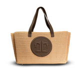 Beige straw tote bag with brown leather handles and logo on a white background