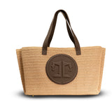 Beige straw tote bag with brown leather handles and logo on a white background