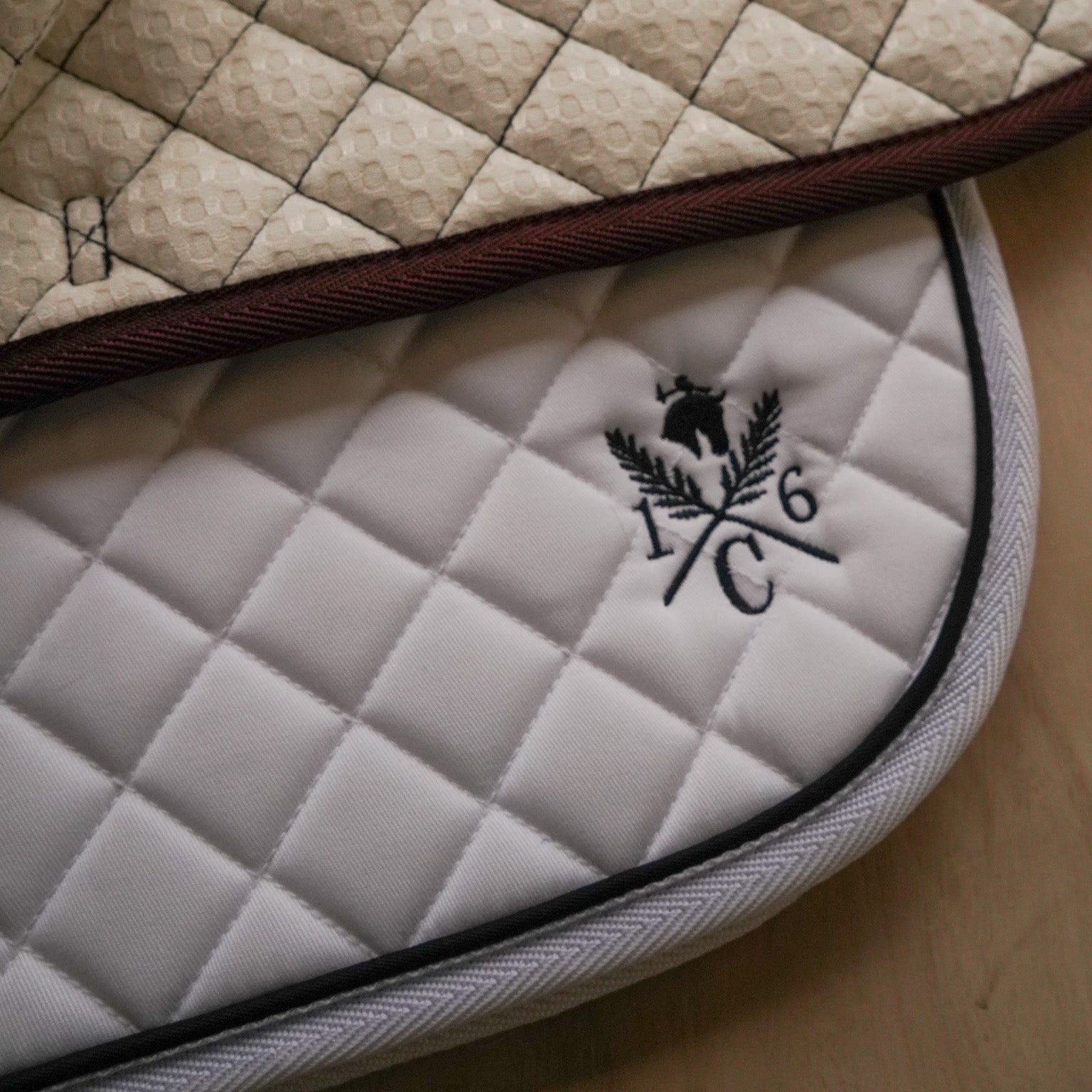Close-up of a quilted saddle pad with a logo on a wooden surface