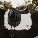 Black and white saddle on a horse with trees in the background. Sixteen Cypress