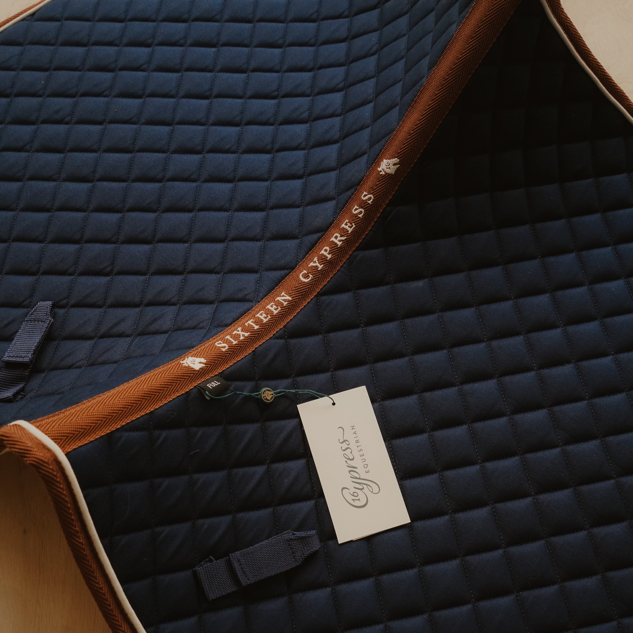 Navy quilted saddle pad with brown trim and Cypress Equestrian tag.