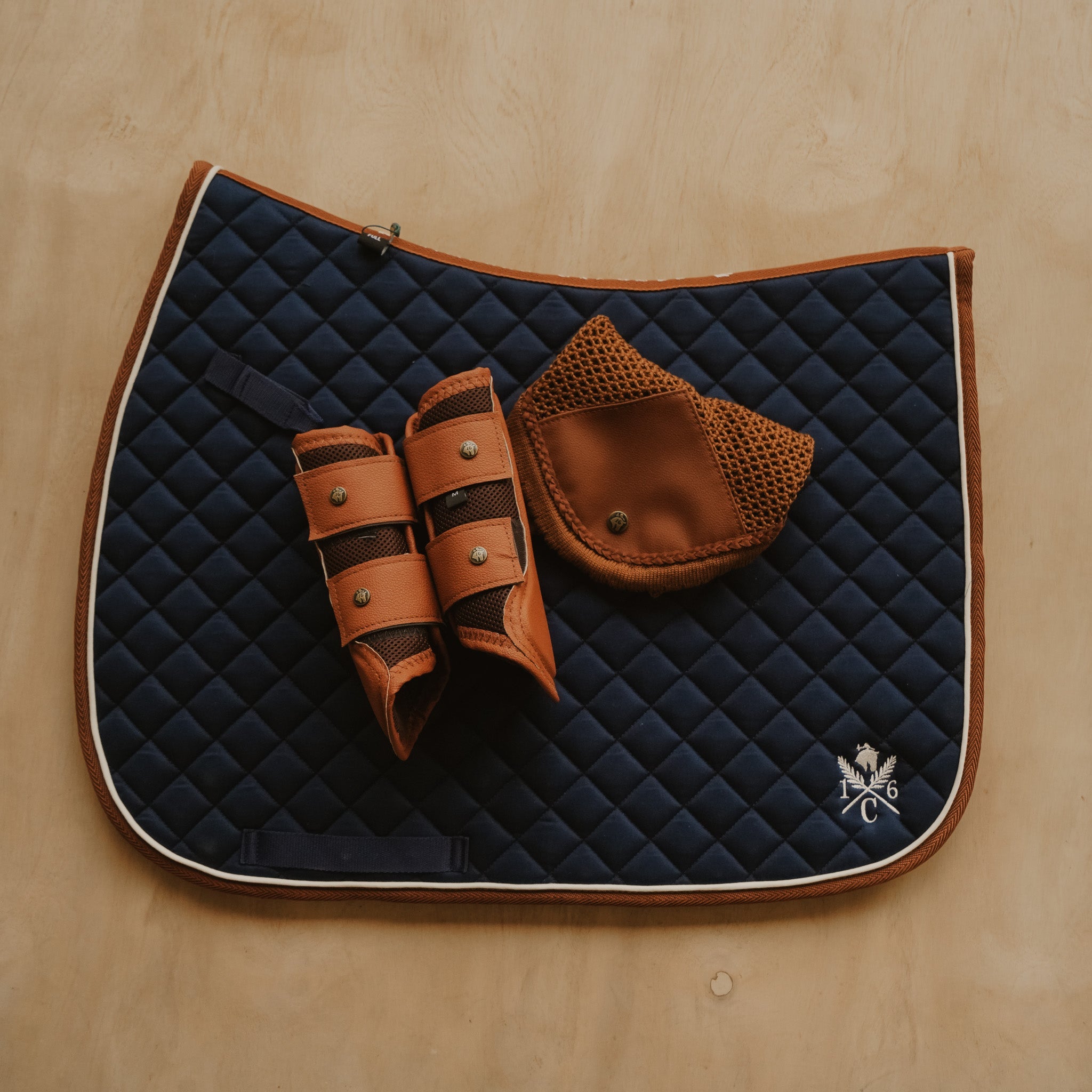 Navy quilted saddle pad with brown leather accessories on a wooden surface