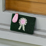 Green clutch with beads on a wooden surface. Features Tucker Tweed's signature equestrian style